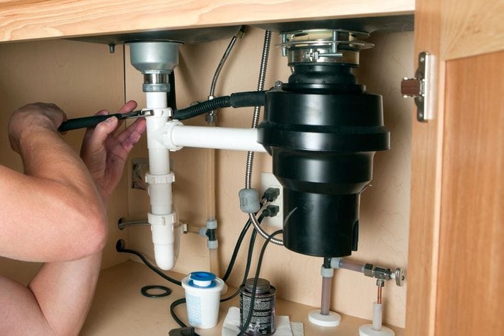 Plumber installing a garbage disposal beneath a kitchen sink in Greeley